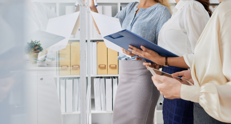A group of professionals with clipboards, and a tablet standing together in an office/planning setting