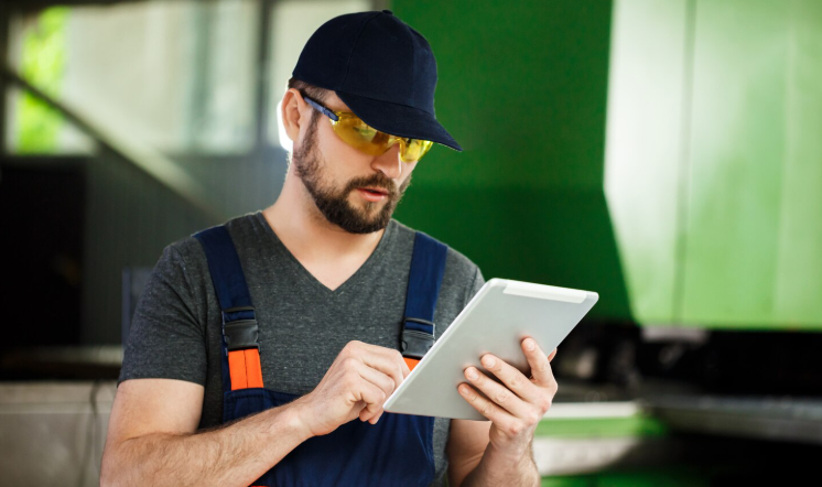 A worker in safety gear checking a tablet in an industrial/plant setting