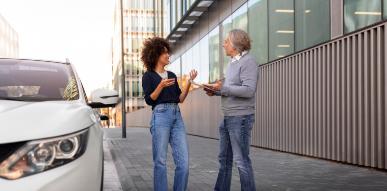 Two people talking casually next to a car on a city street