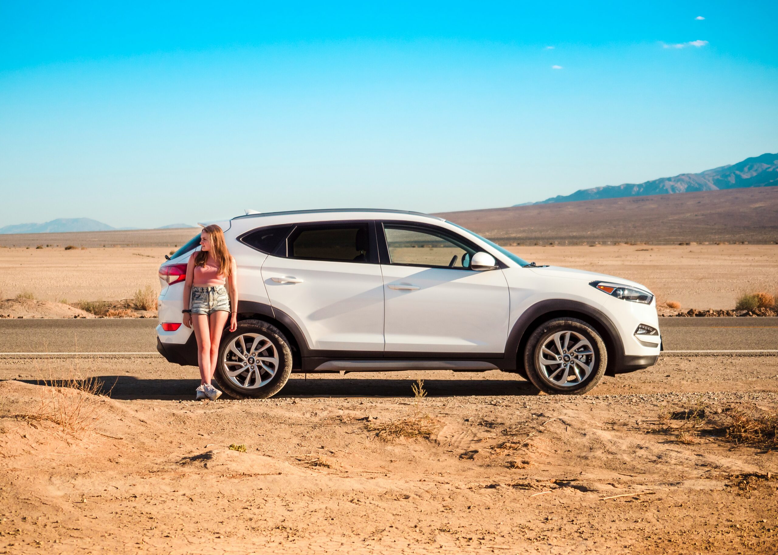Woman leaning against a white SUV in a desert landscape