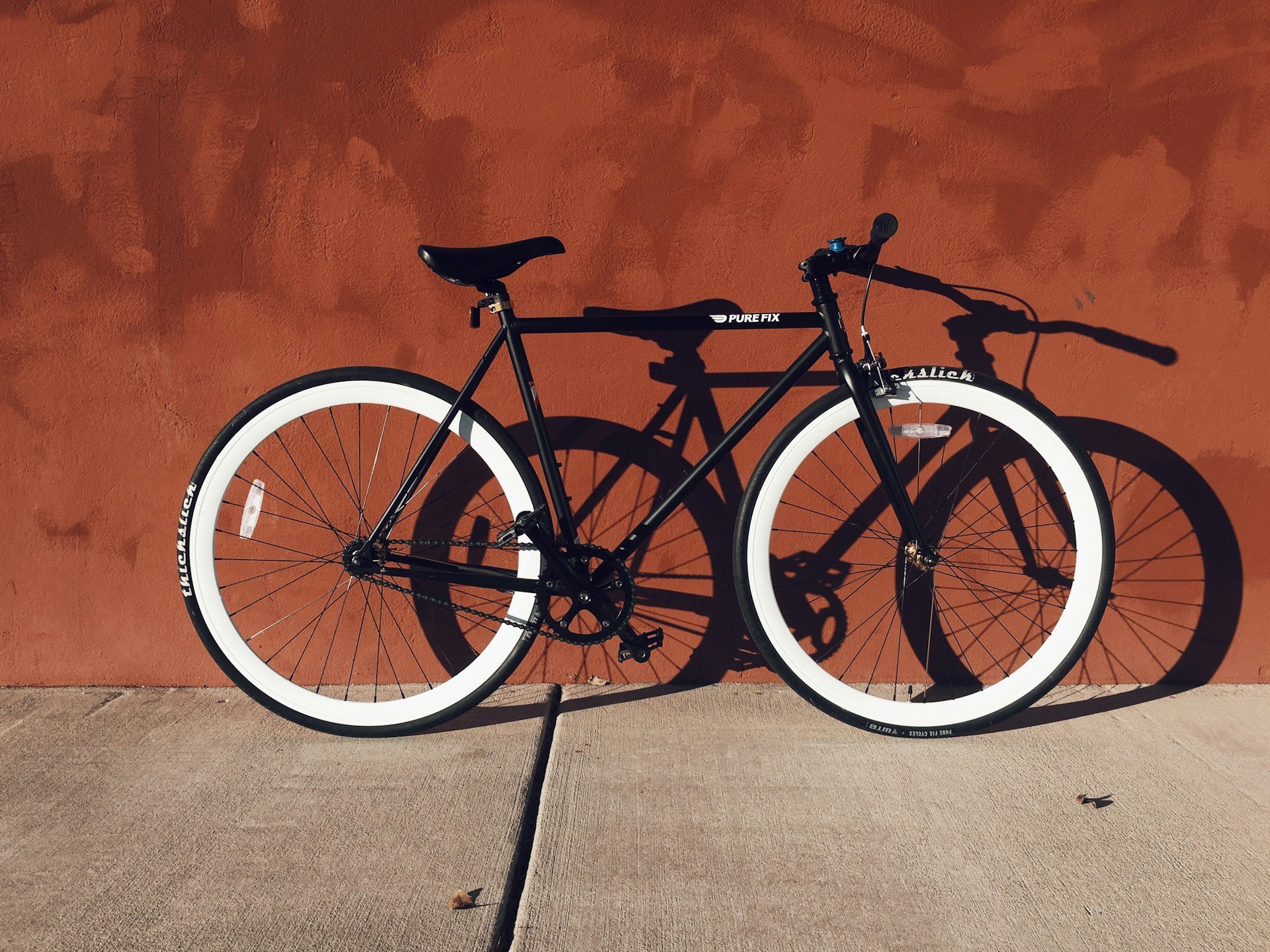 Black fixie bicycle with white tires leaning against a terracotta wall