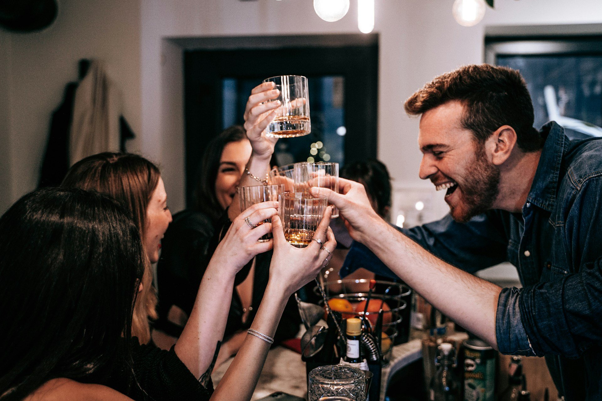 Group of friends cheering and clinking whiskey glasses at a party