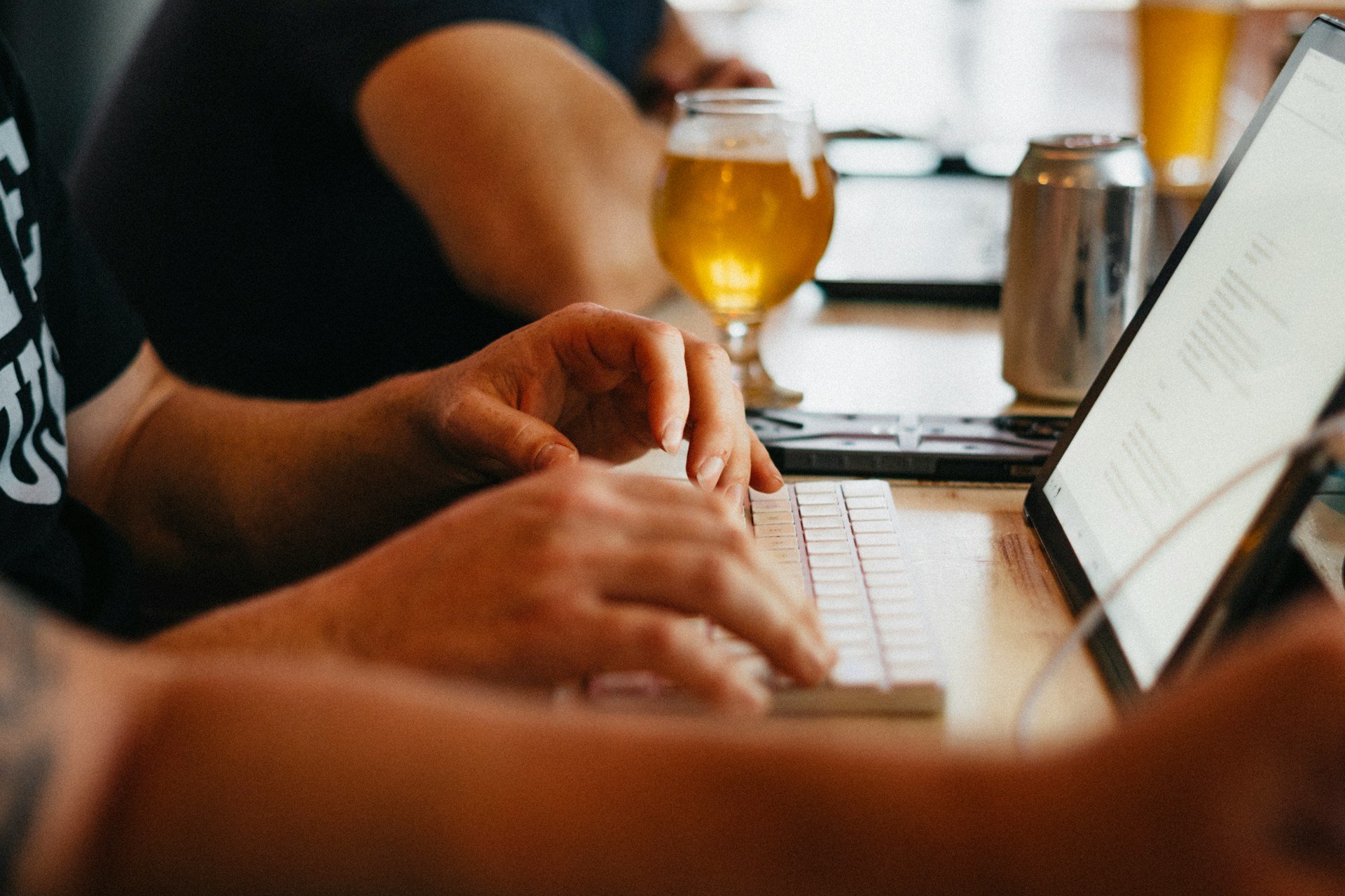 Hands typing on a keyboard with beer and laptop during remote work