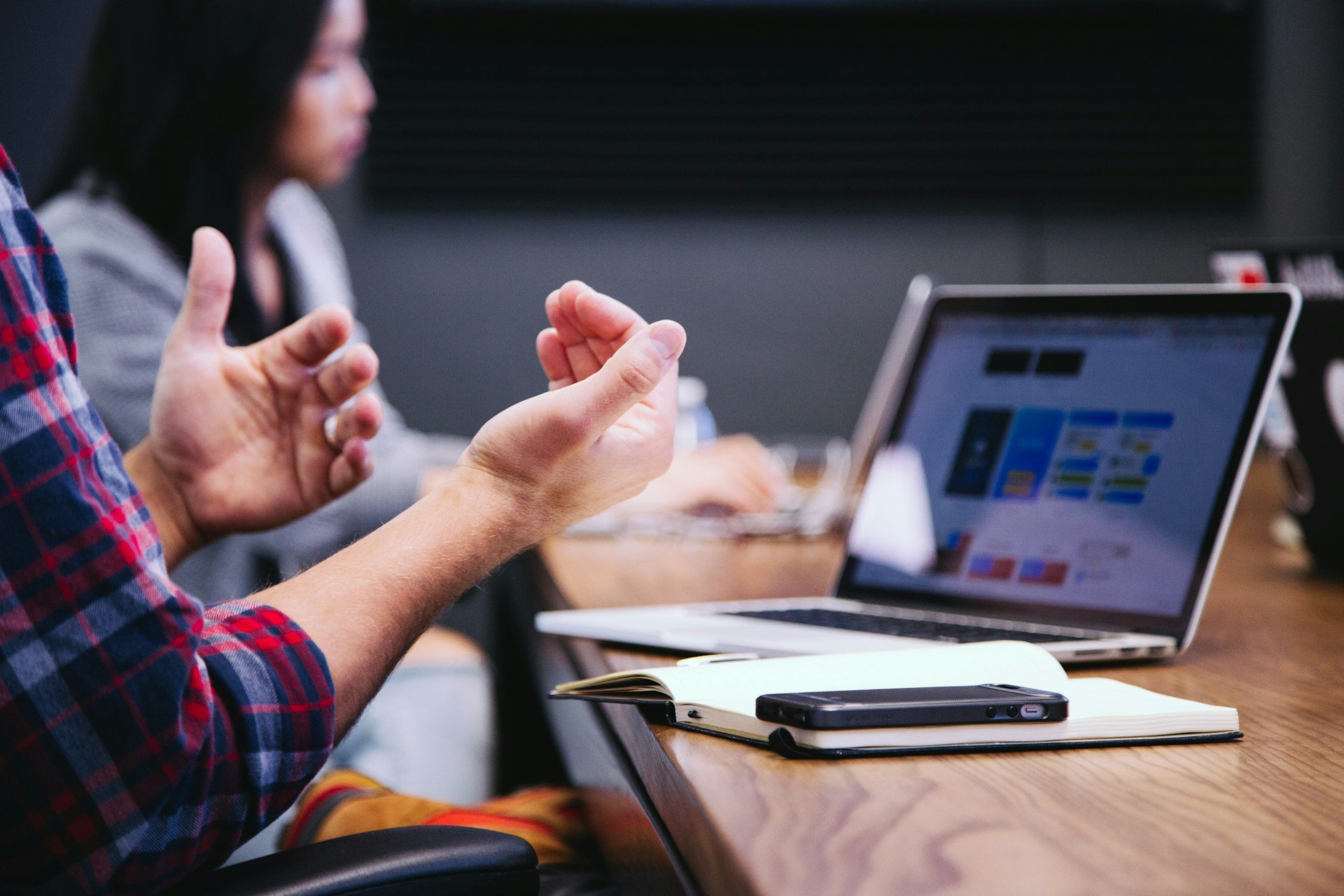 Person gesturing while talking in a business meeting with a laptop and notebook