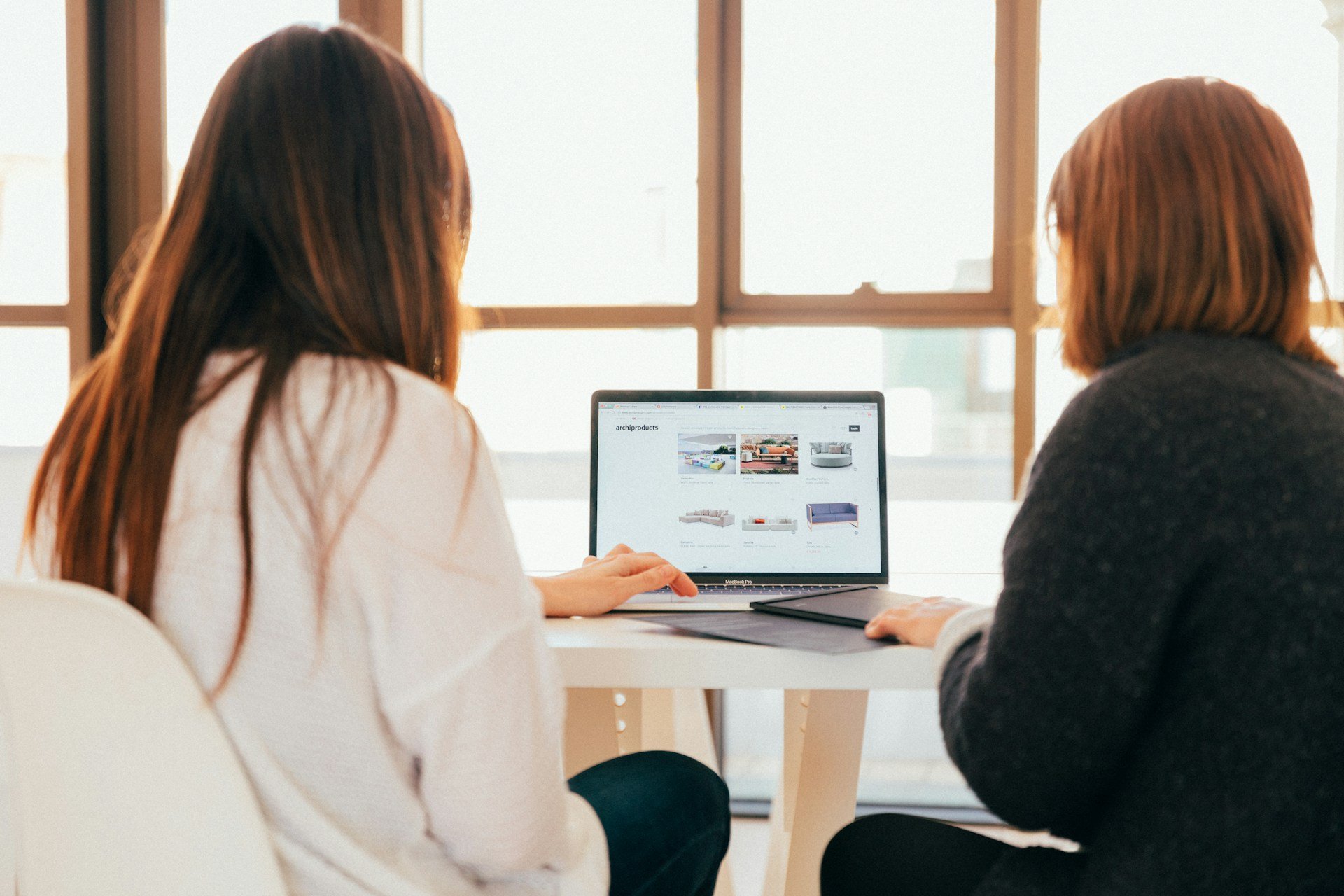 Two women looking at furniture designs on a laptop screen