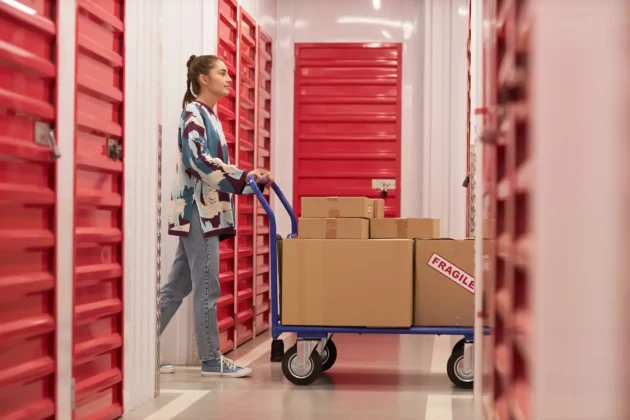 Customer moving boxes on a cart inside a self storage facility with red storage units and secure indoor corridors