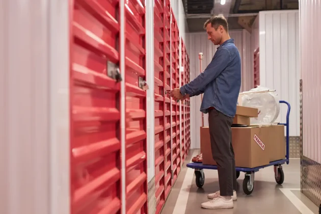 Customer unlocking a red self storage unit while standing next to a cart with packed boxes